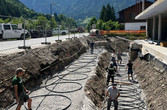 Baustellenbild mit mehreren Arbeitern, die ein Kunststoffrohr in Schlaufen verlegen
