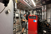 Heizraum mit Wärmepumpengerät, Arbeiter beim Dämmen der Rohrleitungen