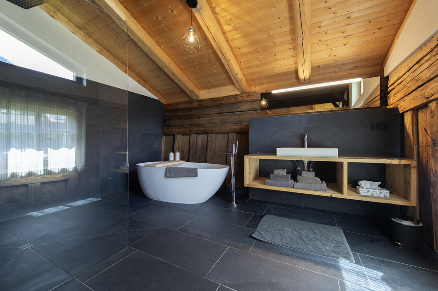 Badezimmer mit dunklen Fliesen, freistehender Badewanne und Waschtisch