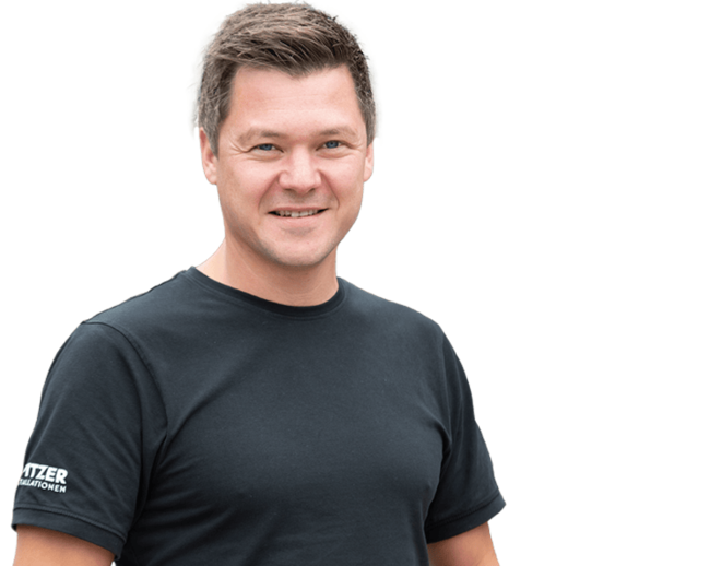 Walter Spitzer, Geschäftsführung – Spitzer Installationen, Feldkirchen Walter Spitzer, Geschäftsführung, in rotem T-Shirt, hält einen Zollstab, der die Form eines Hauses hat