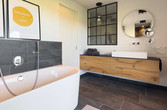Das Badezimmer mit Badewanne, Möbelwaschtisch und Fenster zum Nebenraum