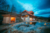 Das beleuchtete Chalet Kaiser mit Schwimmteich und Saunahütte in der Abenddämmerung